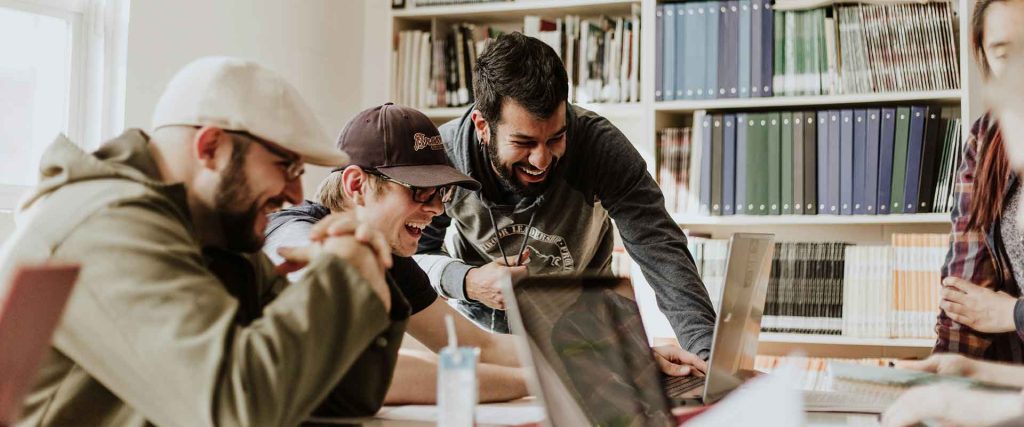 Jóvenes en una biblioteca riendo frente a un ordenador. Foto de Priscilla Du Preez en Unsplash